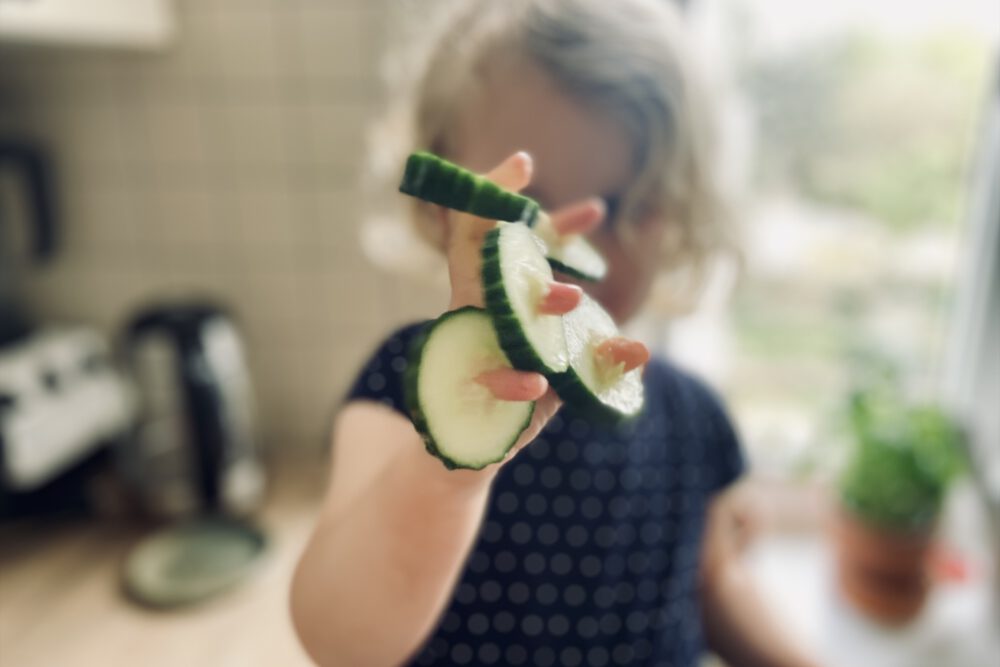 Kleinkind hat an jedem Finger eine Gurkenscheibe aufgefädelt