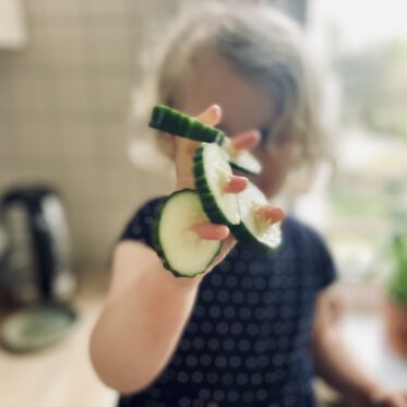 Kleinkind hat an jedem Finger eine Gurkenscheibe aufgefädelt