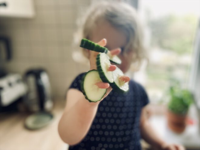 Kleinkind hat an jedem Finger eine Gurkenscheibe aufgefädelt